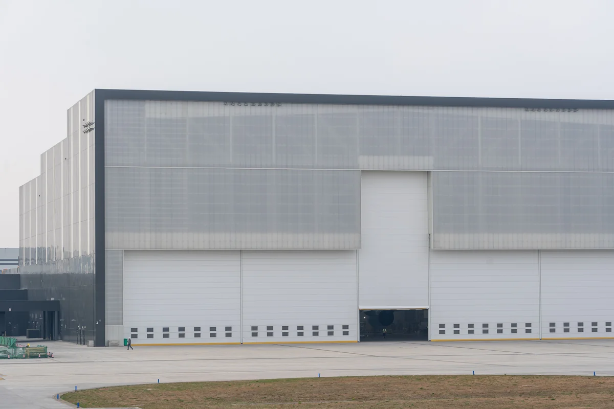 Wide landscape view of a large modern white industrial warehouse with several closed loading doors and one open bay.