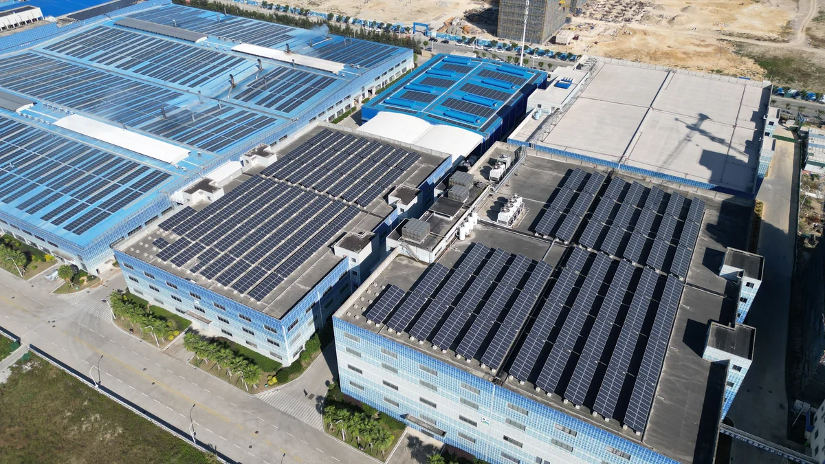 Aerial view of industrial buildings with extensive rooftop solar panel arrays, access roads, and landscaped plantings.