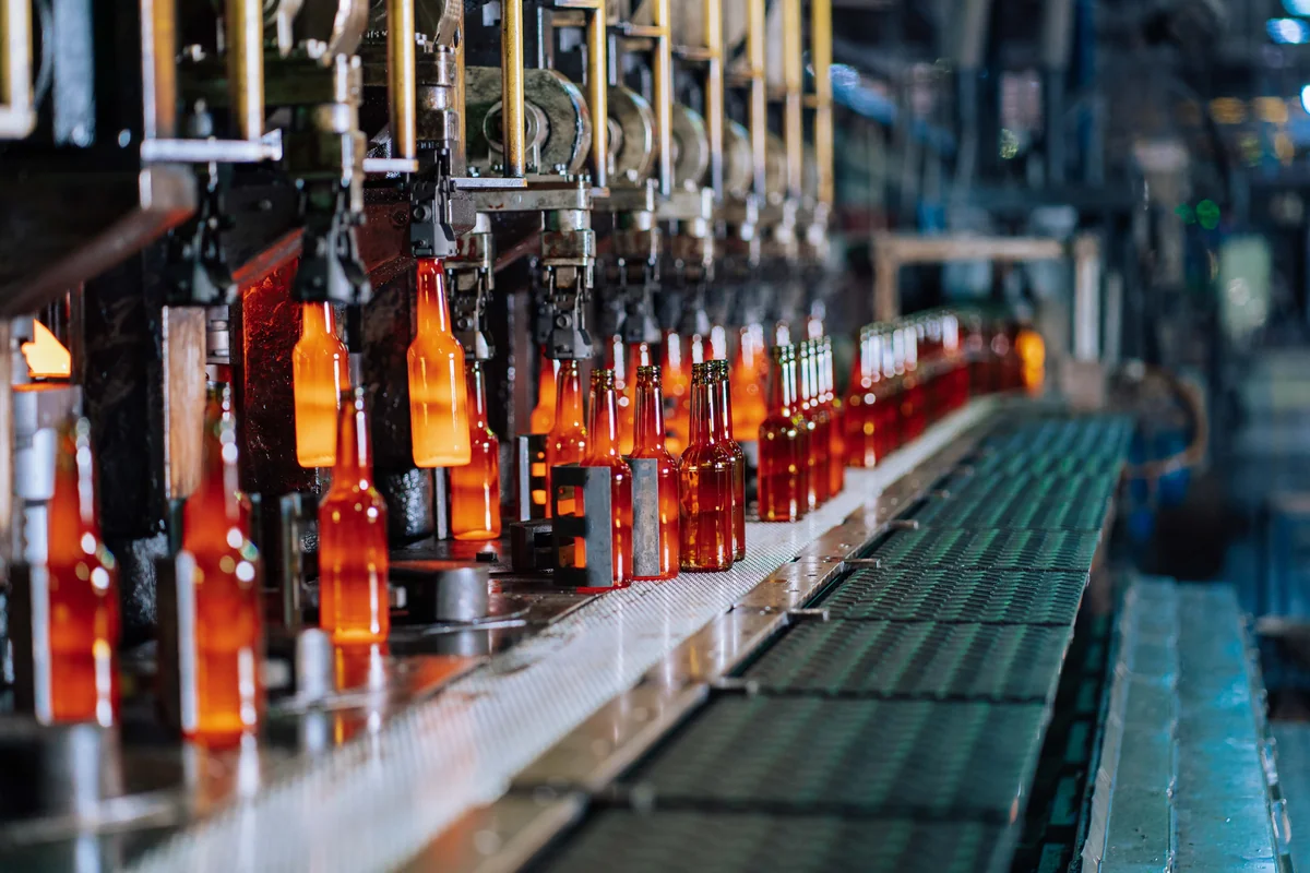 Automated glass bottle production line with rows of orange bottles moving through industrial forming machinery.