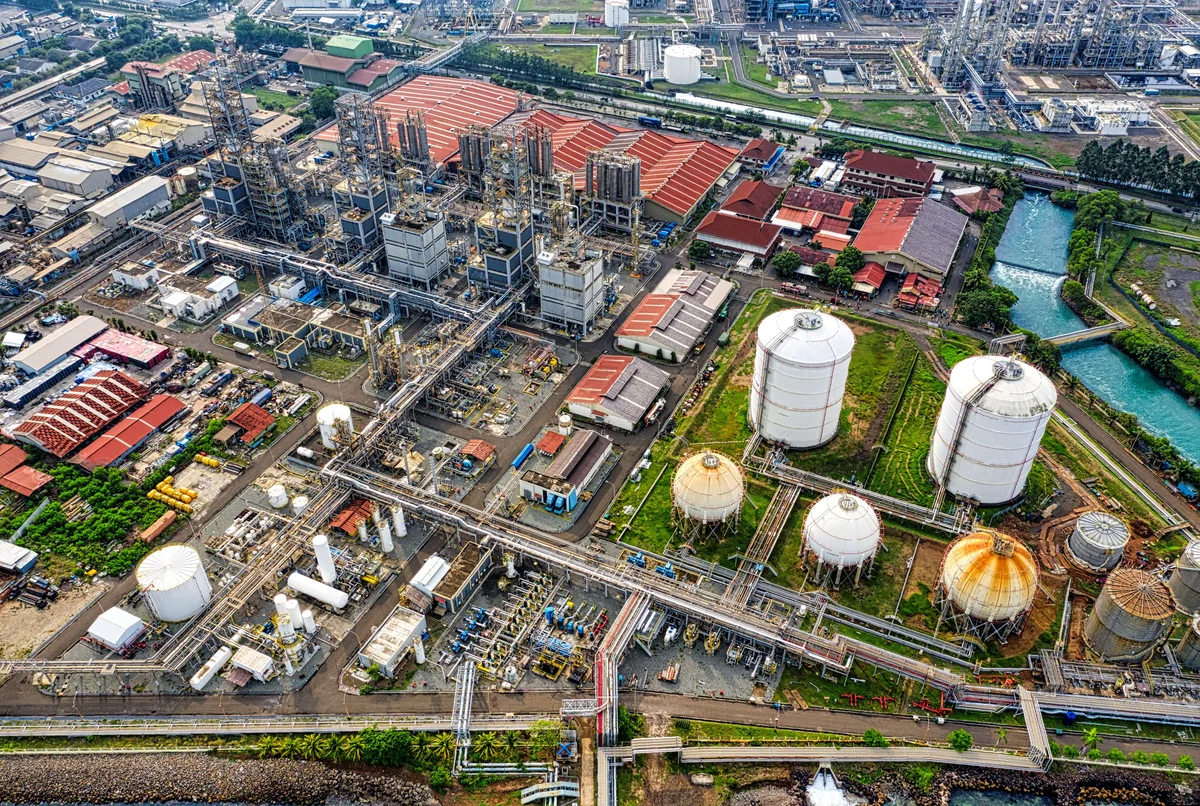 Aerial view of an industrial facility with processing structures, storage tanks, pipelines, rail lines and a canal.