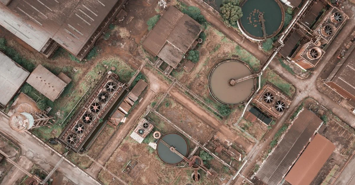 Aerial view of circular settling tanks, rectangular treatment basins, industrial buildings, pipes and access roads in a wastewater treatment facility.