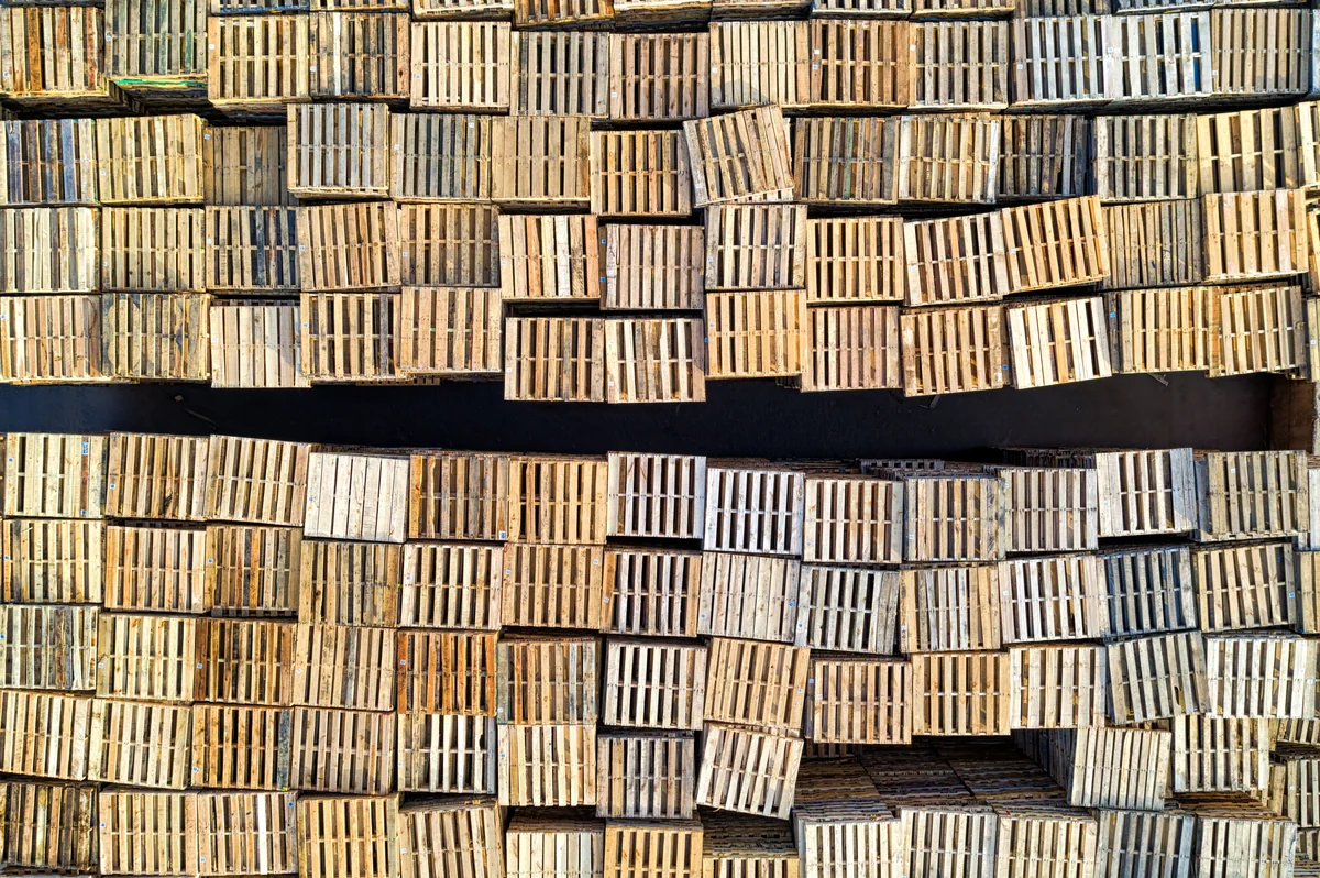 Aerial view of tightly arranged stacks of weathered wooden pallets in an outdoor industrial storage yard.