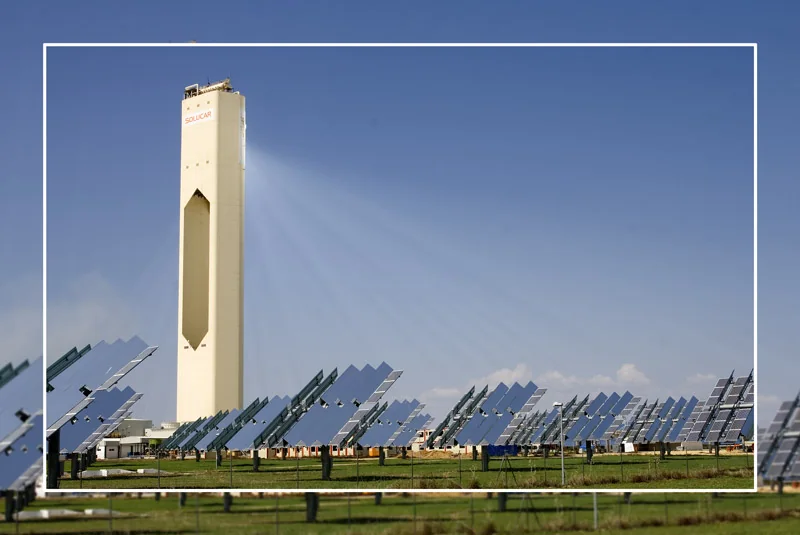 Solar thermal power tower surrounded by rows of mirrored collectors under a blue sky.