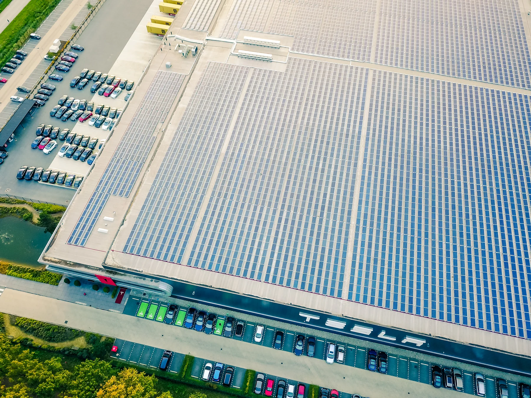 Aerial landscape photograph of rows of solar panels covering the roof of an automobile assembly plant, with surrounding industrial buildings and roads visible.