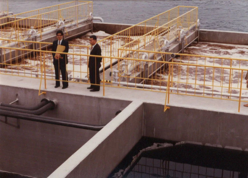 A landscape view of a wastewater treatment plant with rectangular treatment basins, channels and surrounding greenery.