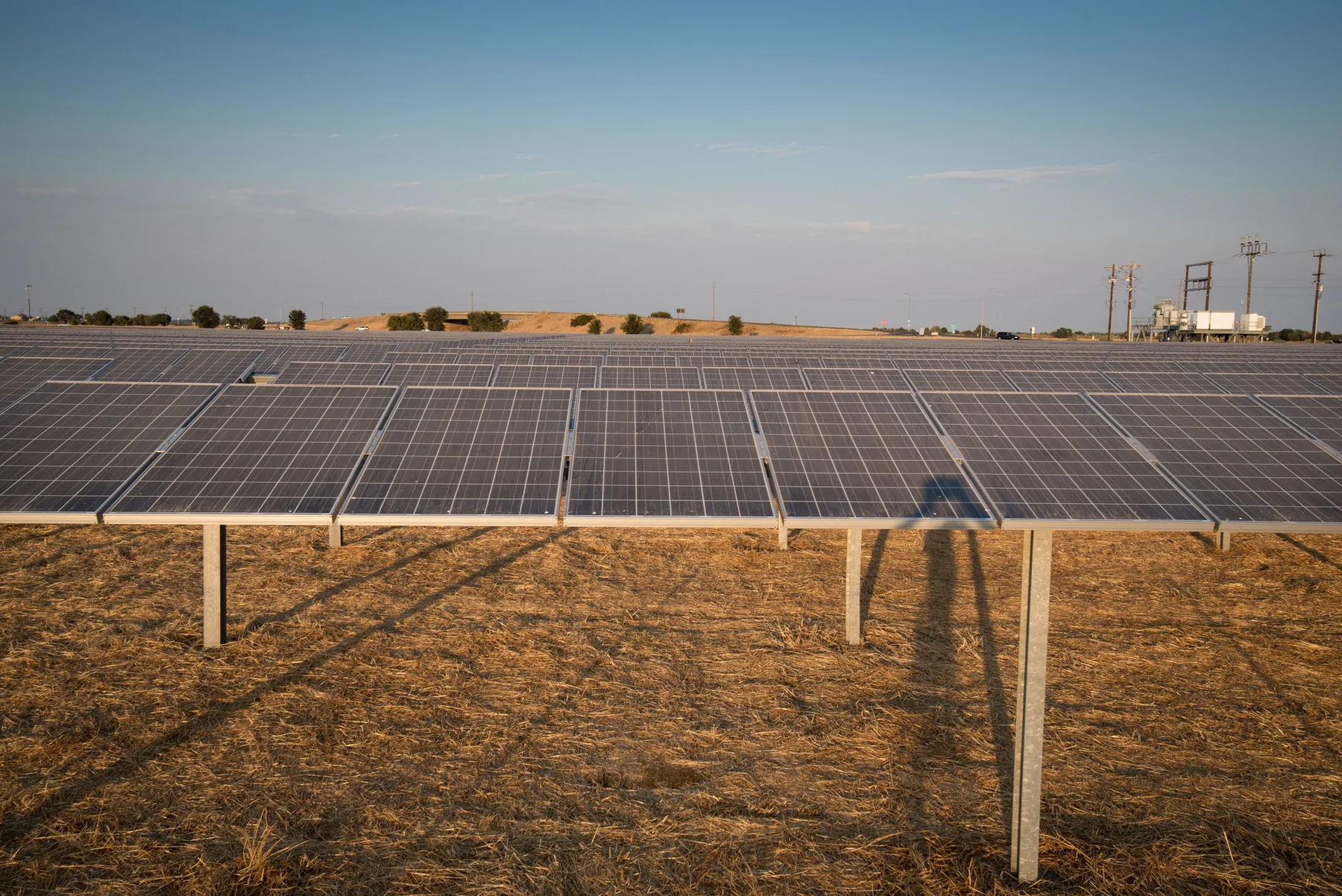 Rows of dark photovoltaic solar panels forming a large power station across an open landscape under a pale sky.