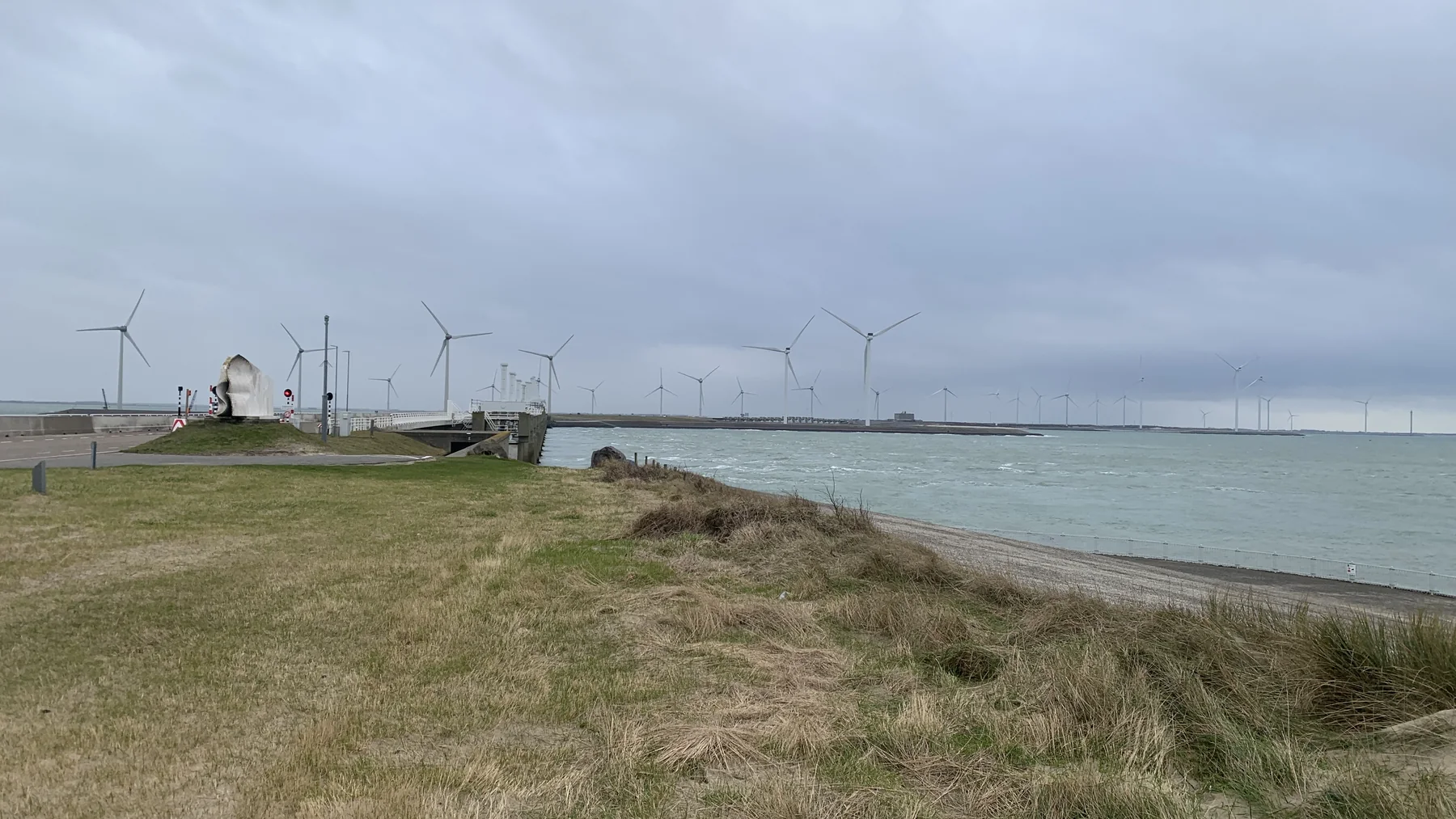 Wide landscape view of the Oosterscheldekering storm-surge barrier across coastal water, with a low sandy shoreline and open sky in the distance.