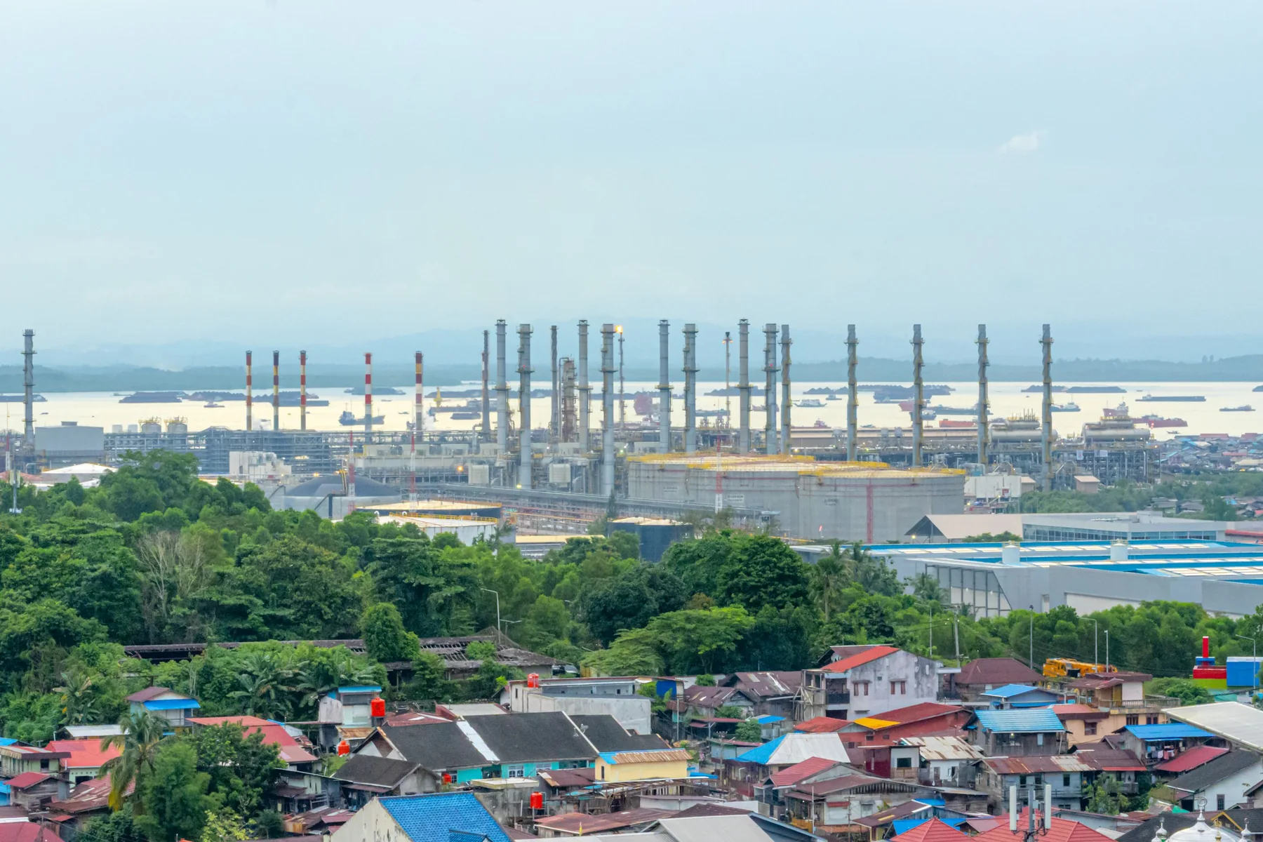 Aerial landscape view over an industrial area in Balikpapan, with factory buildings surrounded by green vegetation.