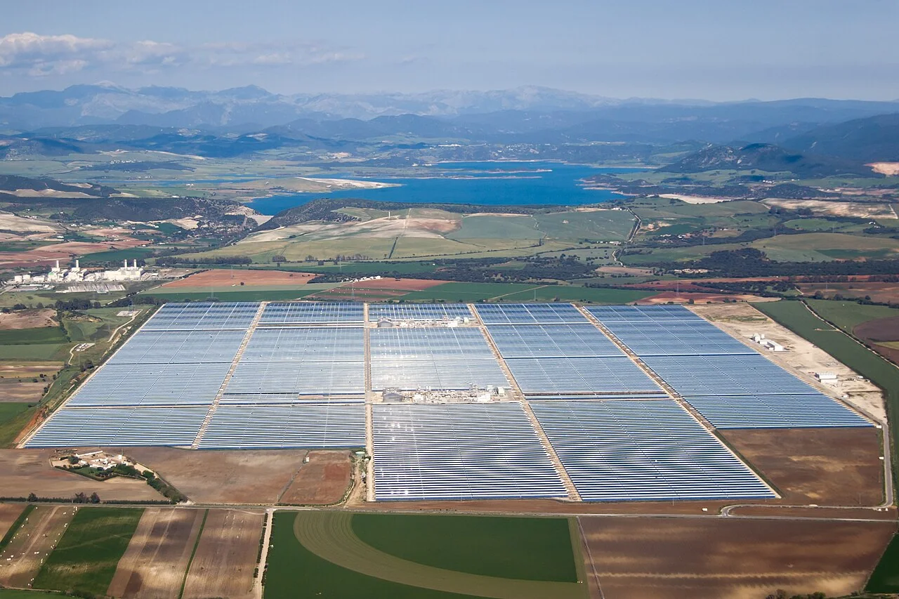 A broad field of photovoltaic panels at Valle 1 and Valle 2 Solar Power Station beneath a blue sky.