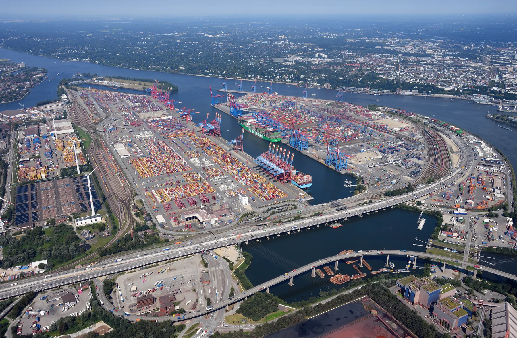 Aerial landscape photograph of rows of shipping containers, cranes, rail lines and waterways at the Eurogate and Burchardkai container terminals in Hamburg.