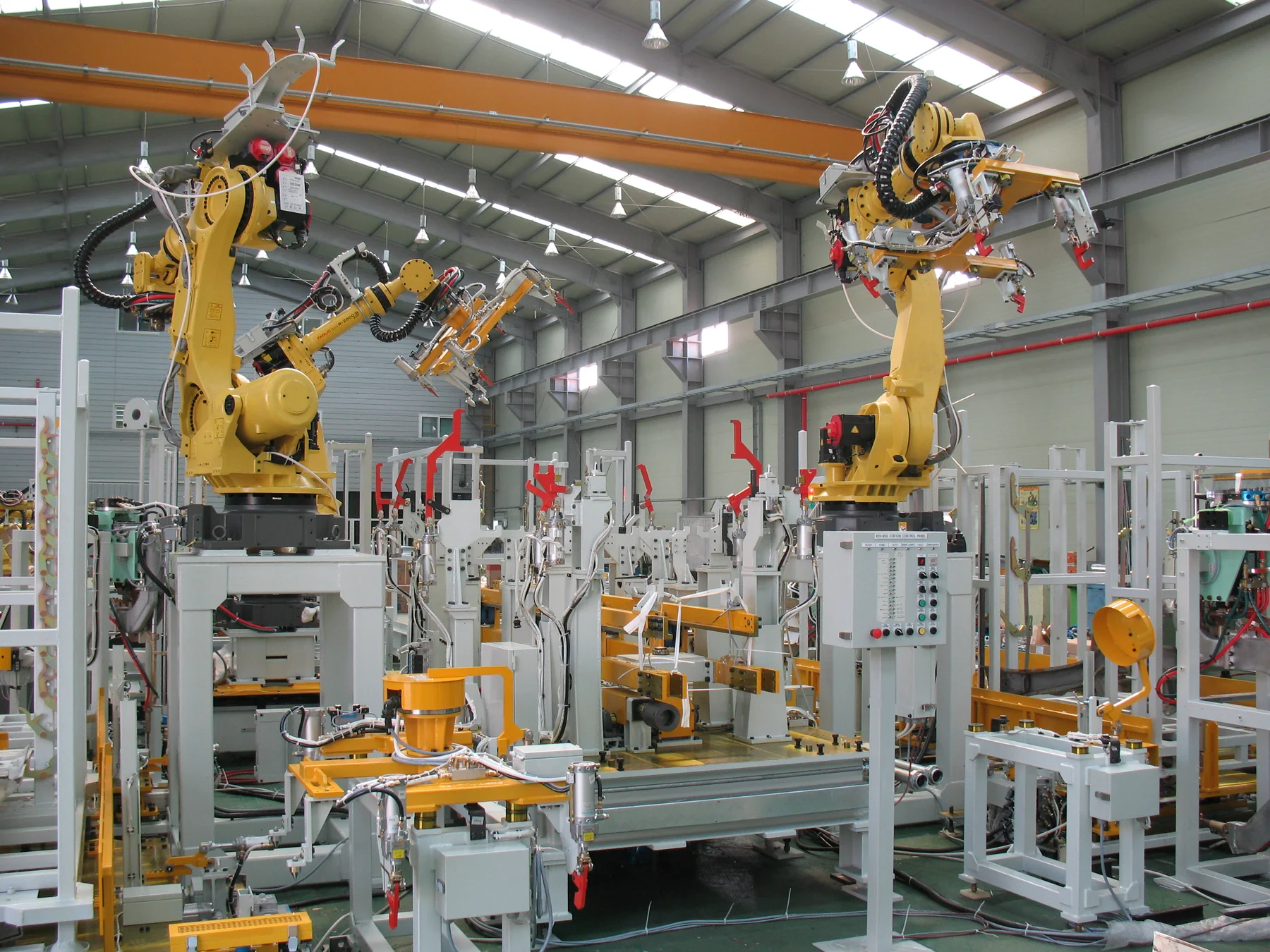 Landscape photograph of a clean industrial assembly hall filled with yellow robotic arms, conveyors, fixtures, control panels and overhead lighting; no people are visible.