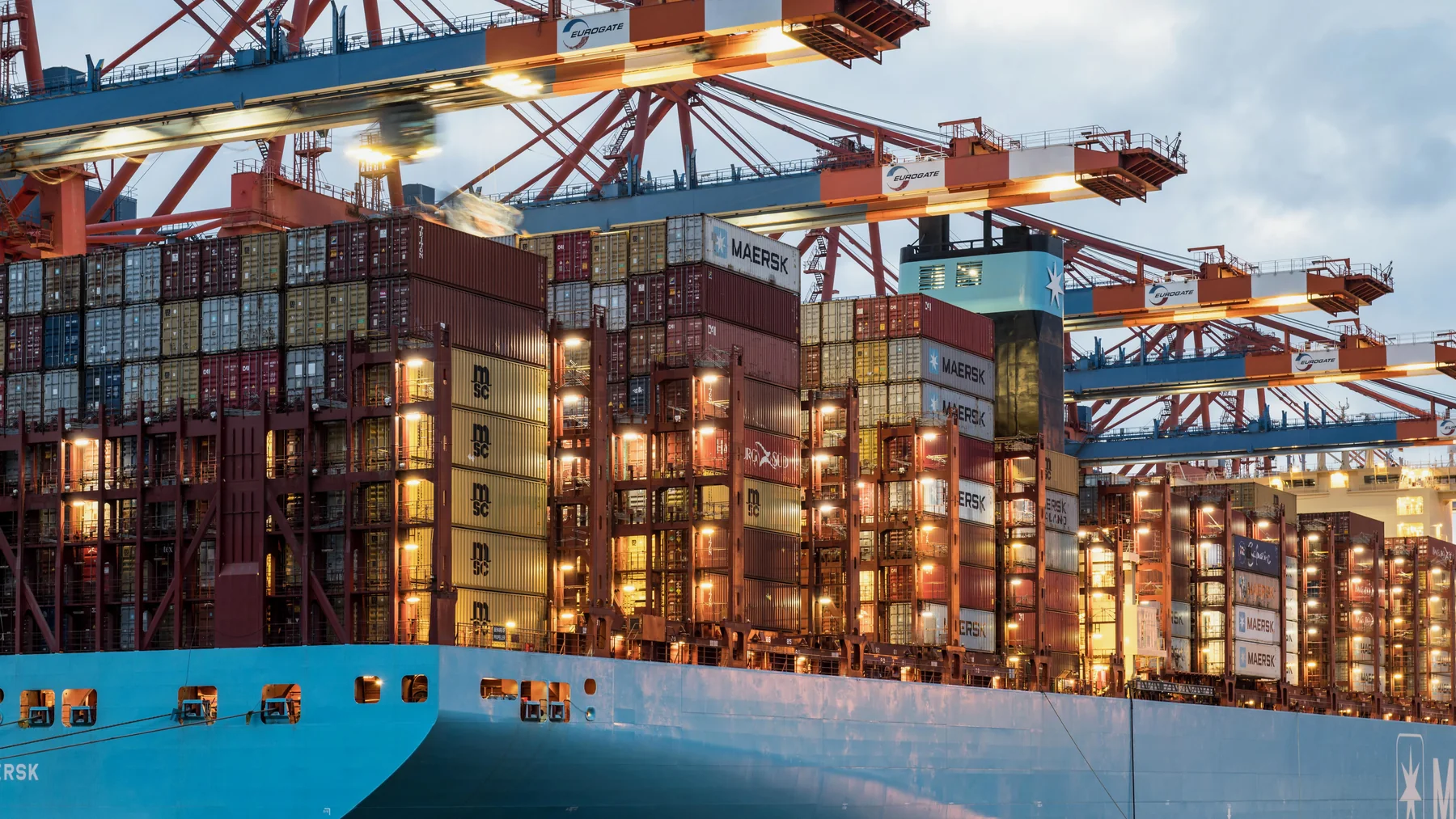 A cargo ship loaded with colorful shipping containers beside cranes at a harbor.