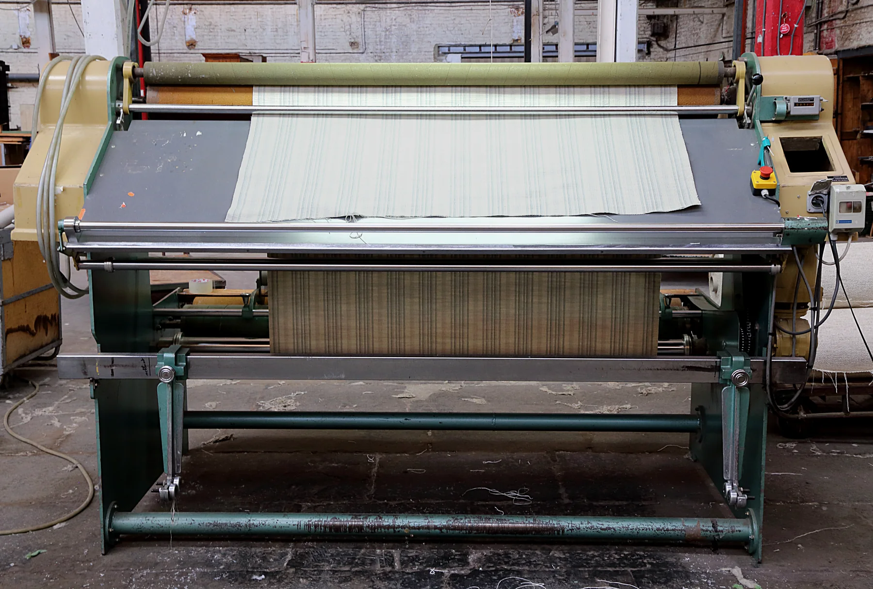 Landscape photograph of a fabric inspection machine and work area in a former textile factory, illustrating a manufacturing workplace context for responsible employment practices.