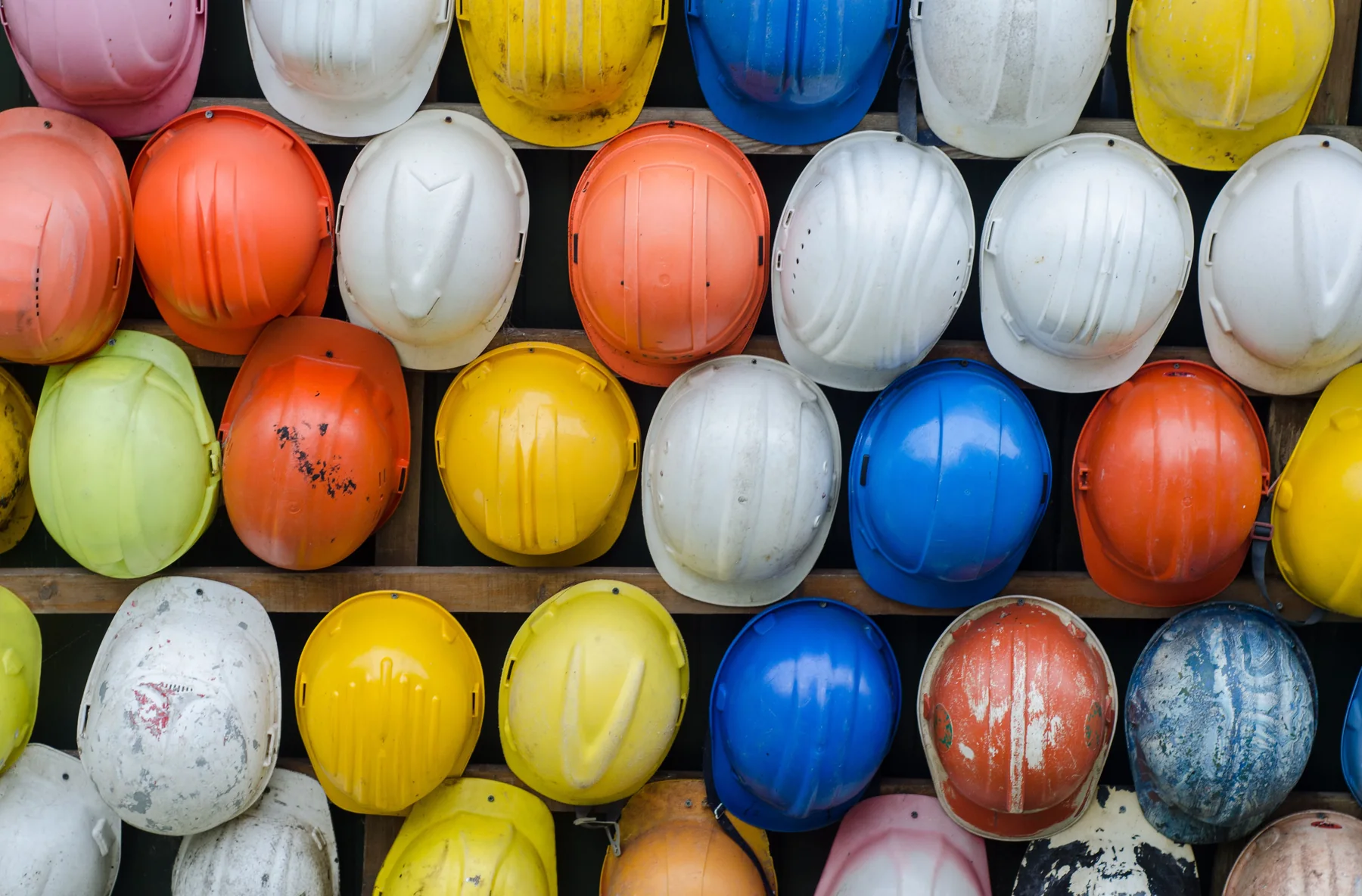 Several yellow industrial safety helmets arranged in rows against a dark workshop wall.