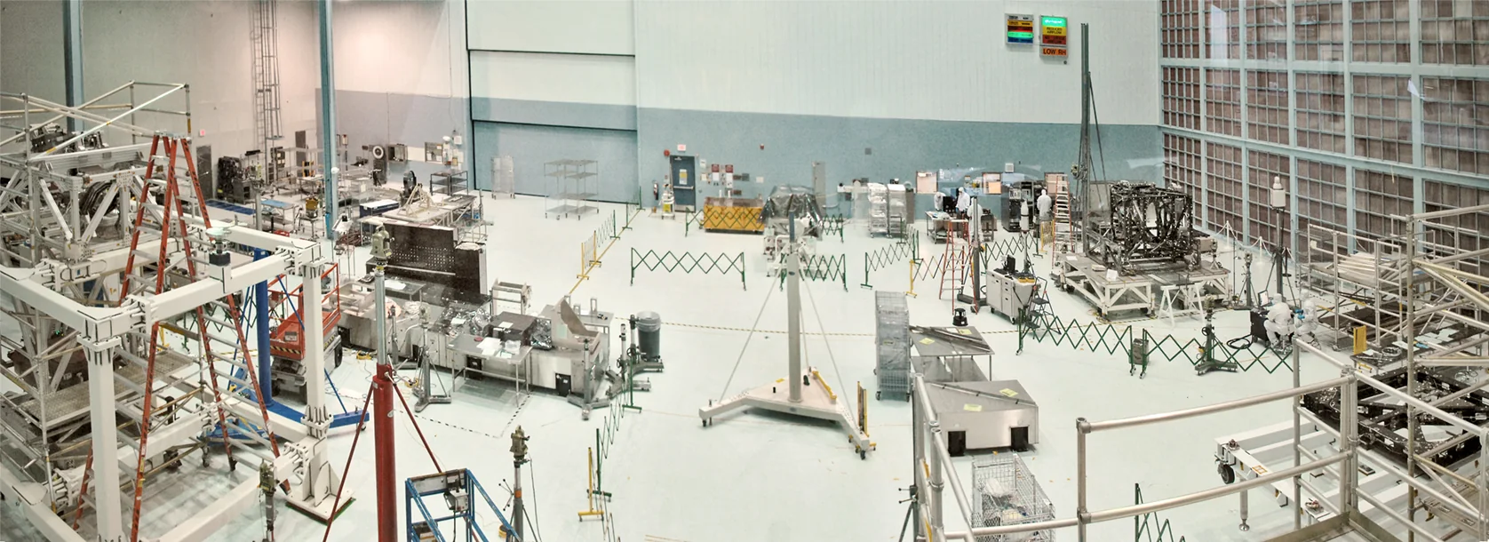 Panoramic interior of a high-bay clean room with bright ceiling lights, white structural surfaces, and industrial equipment behind viewing windows.