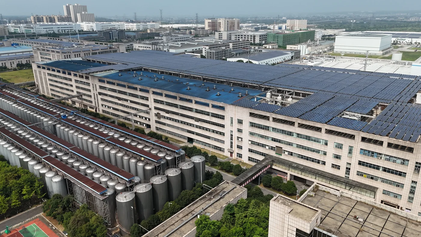 An industrial building covered with rooftop solar panels beside storage tanks.