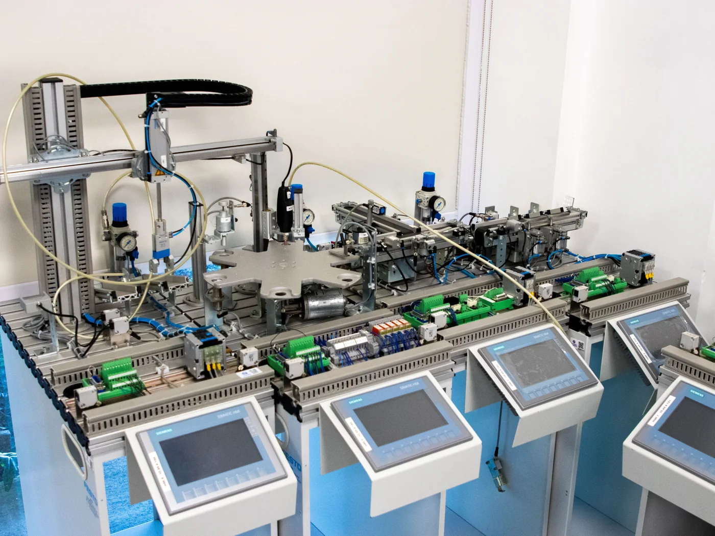 Bright industrial automation system with pneumatic lines, sensors, wiring, conveyor fixtures and touchscreen control panels in a laboratory.