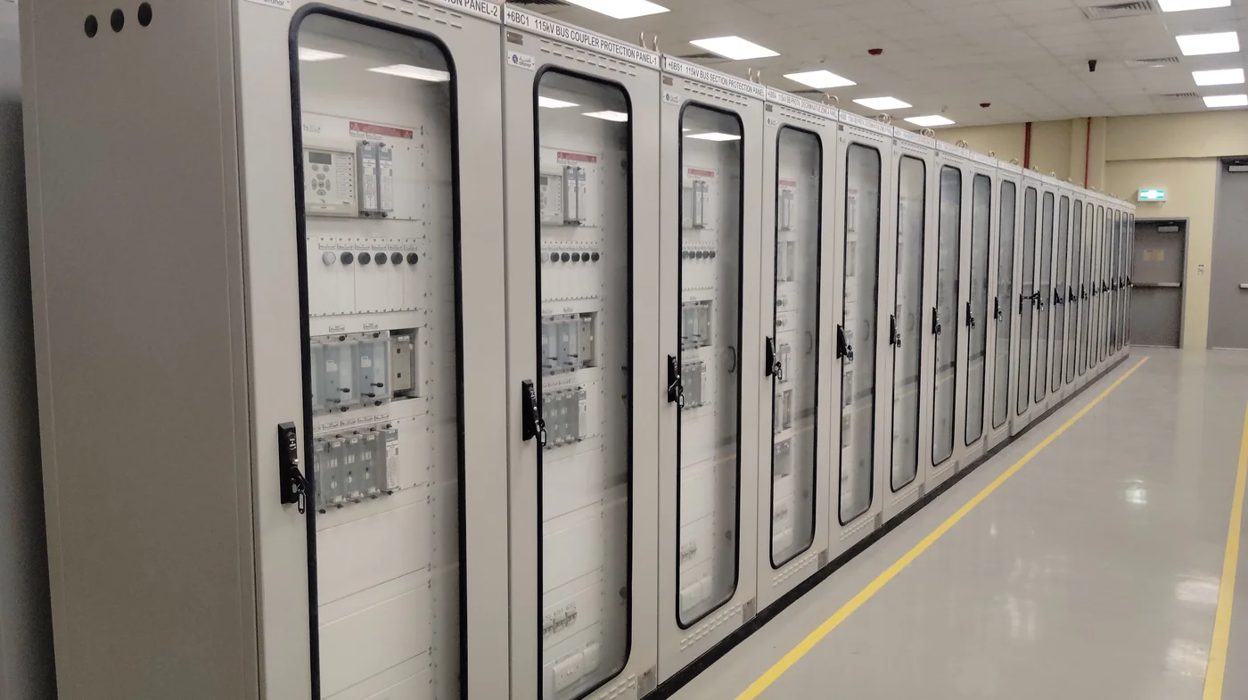 Bright, empty industrial control room with a long row of electrical panels receding into the distance.