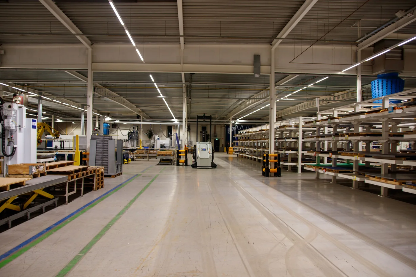 Bright modern industrial warehouse interior with machinery, storage shelves and a wide clean aisle.